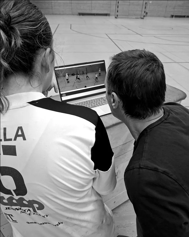 Trainer und Spielerin bei der Videoanalyse am Laptop in der Halle